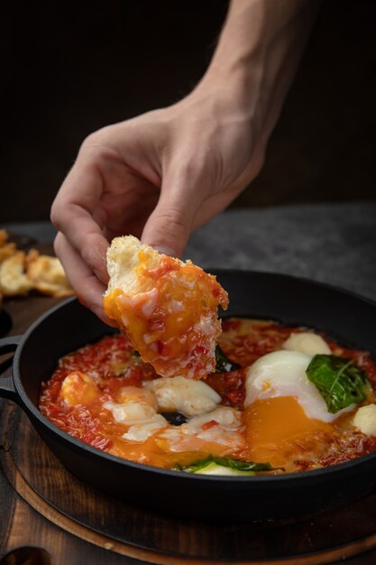 Huevos escalfados, con tomate y salsa en una sartén sobre una tabla de madera