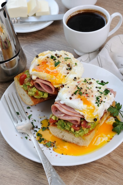 Huevos escalfados con tomates aguacate lonchas de jamón en una baguette para el desayuno