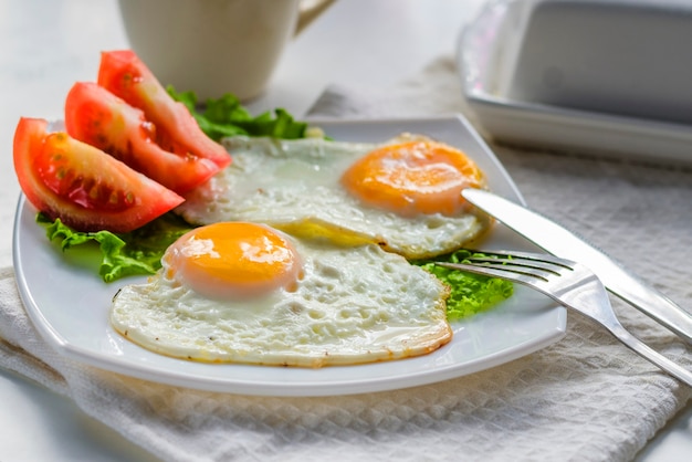 Huevos fritos de dos huevos en un plato con tomate