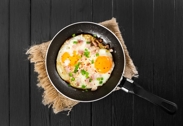 Huevos fritos con jamón y cebolla en sartén sobre fondo de madera negra Vista superior