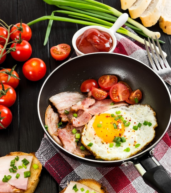 Huevos fritos con jamón y tomates en pan sobre fondo de madera negra