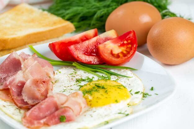 Huevos fritos con jamón y tomates en un plato blanco