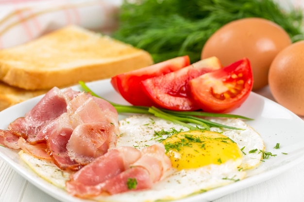 Huevos fritos con jamón y tomates en un plato blanco