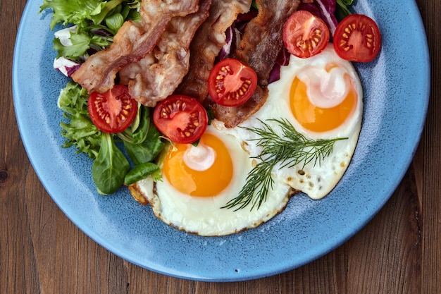 Huevos fritos en una placa azul con tocino, lechuga y tomates cherry