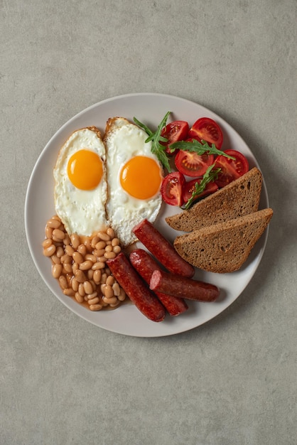 Huevos fritos con salchichas y frijoles en un plato sobre un fondo gris Desayuno inglés