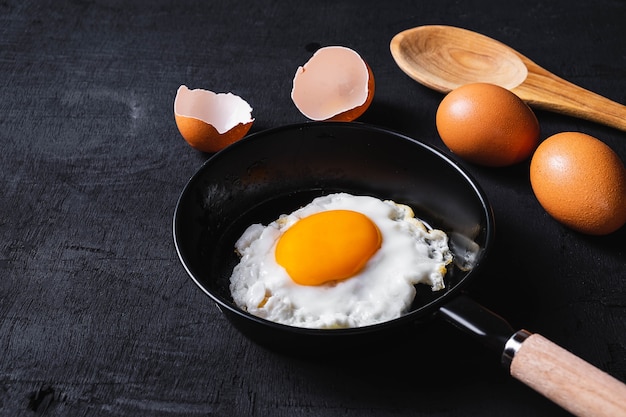 Huevos fritos en una sartén y una cáscara de huevo para el desayuno en un fondo negro.