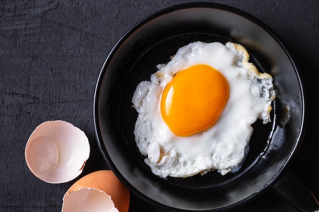 Huevos fritos en una sartén y una cáscara de huevo para el desayuno en un fondo negro.