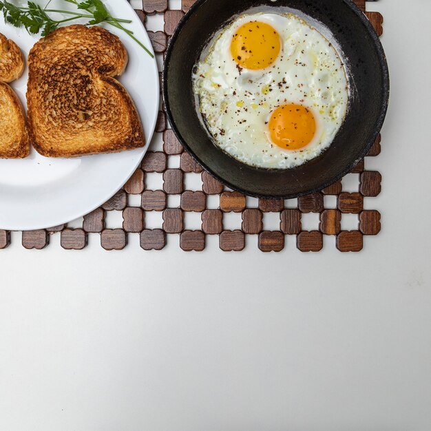 Huevos fritos en una sartén de hierro rústico, tostadas en un plato para el desayuno. Copie el espacio. Vista superior.