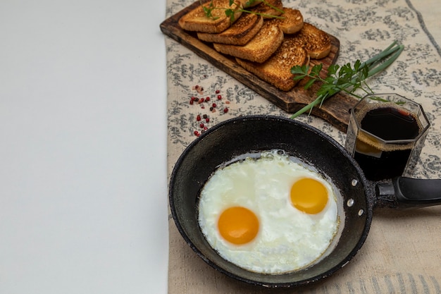 Huevos fritos en una sartén de hierro rústico, tostadas sobre una tabla de madera y una taza de café para el desayuno.