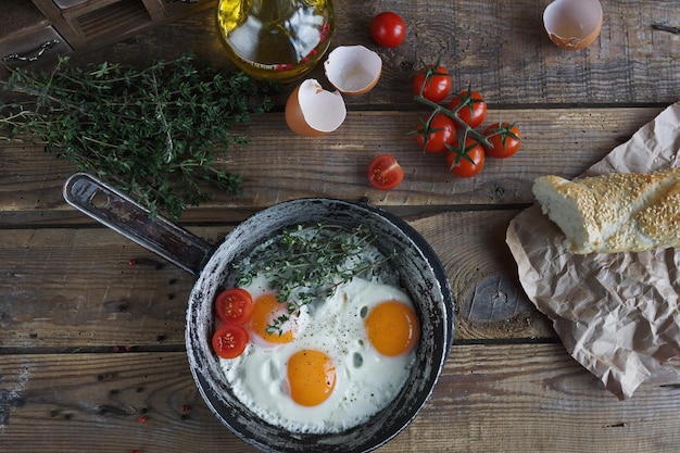 Huevos fritos en una sartén vieja con pan, tomates cherry, aceite de pimienta y tomillo en una mesa de madera