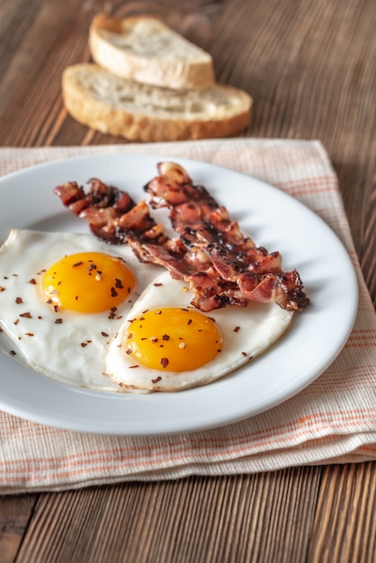 Huevos fritos y tocino en el plato blanco