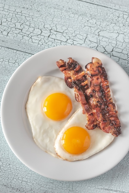 Huevos fritos y tocino en el plato blanco