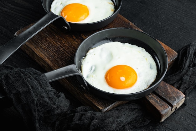 Huevos fritos con tomates cherry y pan para desayunar en sartén de hierro fundido sobre fondo de mesa de madera negra