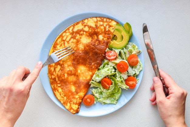 Huevos fritos con verduras. manos en el marco Tortilla de verduras en un plato azul sobre una mesa blanca, vista superior