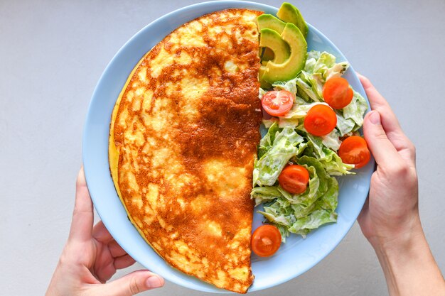 Huevos fritos con verduras. manos en el marco Tortilla de verduras en un plato azul sobre una mesa blanca, vista superior