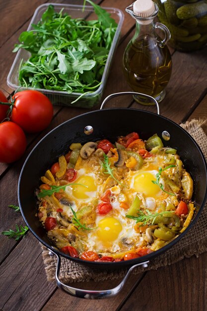 Huevos fritos con verduras en una sartén sobre un fondo de madera