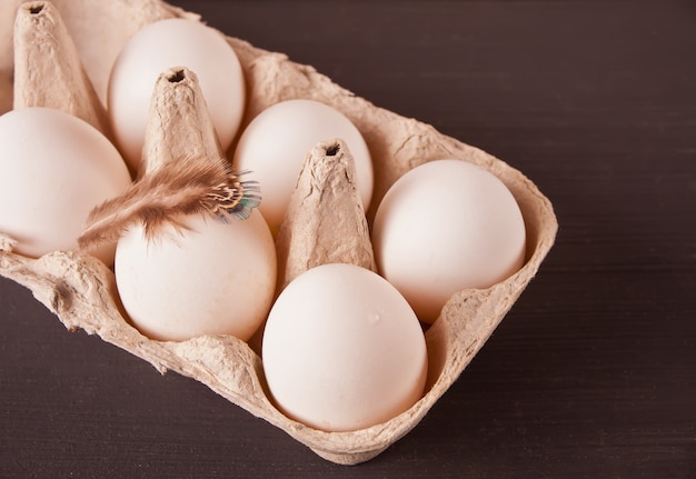 Huevos de gallina blanca en bandeja de papel de huevo con pluma sobre fondo negro