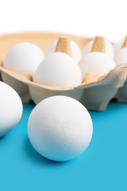 Huevos de gallina blanca en caja de cartón sobre fondo azul.