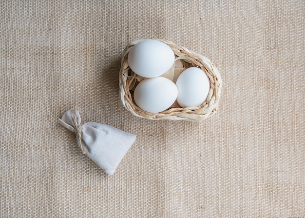 Huevos de gallina blanca en una cesta sobre un mantel de arpillera