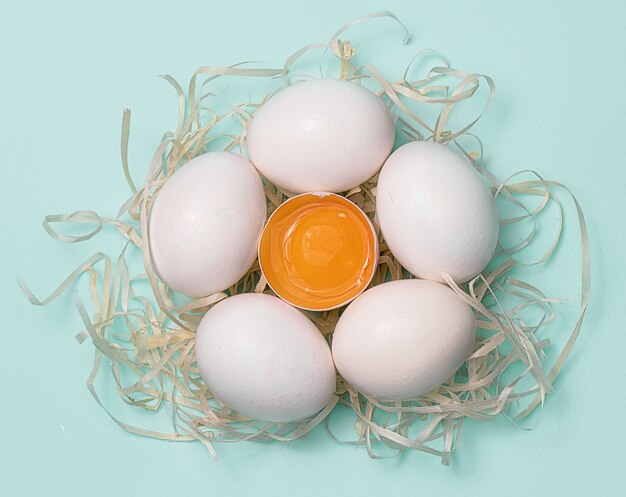 Huevos de gallina blanca en paja sobre un azul