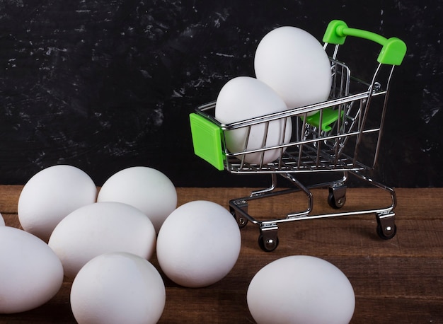 Huevos de gallina blanca sobre la mesa y en la cesta de la compra sobre un fondo negro con copia del espacio.