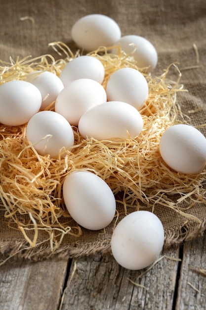 Huevos de gallina blanca sobre paja o heno sobre tela de arpillera y tablas de madera