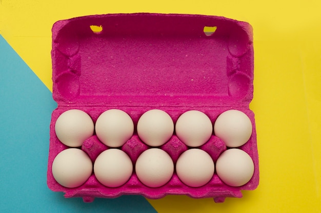 Huevos de gallina en una caja rosa para huevos sobre un fondo amarillo. comprando huevos antes de Pascua.