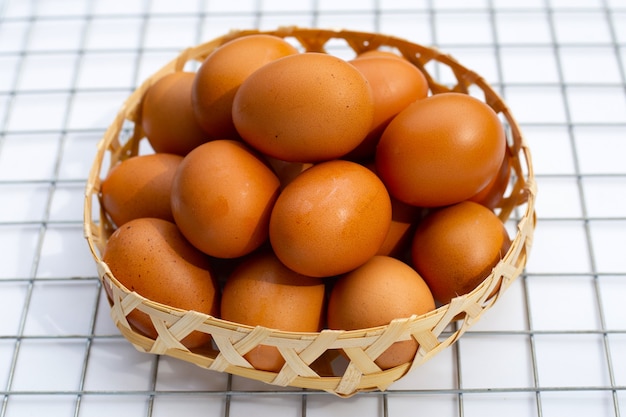 Huevos de gallina en canasta de bambú en blanco.