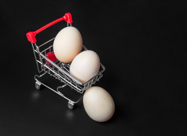 Huevos de gallina en un carrito de compras. Aislado sobre fondo negro. La idea de un comercio exitoso