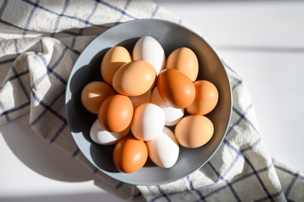 Huevos de gallina de color blanco y marrón en una placa gris sobre una toalla de cocina marcada