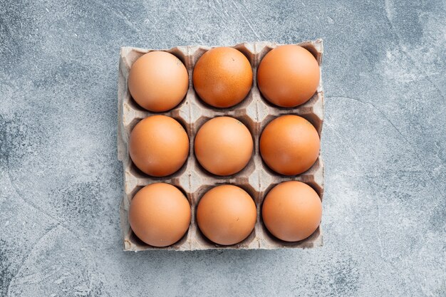 Huevos de gallina crudos en caja de huevos en fondo gris, vista superior plana