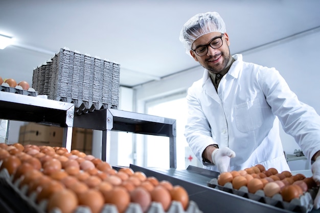 Los huevos de gallina frescos en la fábrica de procesamiento de alimentos se mueven en la cinta transportadora y el trabajador los lleva para el empaque