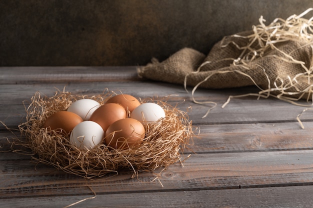 Huevos de gallina marrón y blanca en un nido de paja sobre fondo de madera