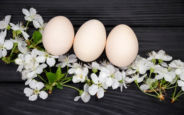 Huevos de gallina orgánicos, bioproductos. Composición de ramas de árboles florecientes. Huevos de Pascua naturales con flores blancas de primavera en la mesa de madera oscura. Concepto de Pascua feliz.