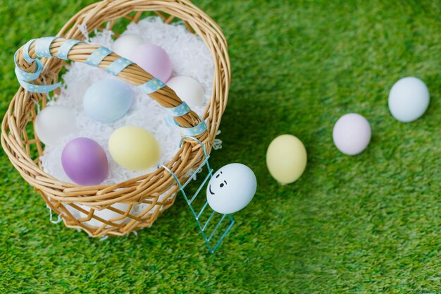 Huevos de gallina de Pascua pintados multicolores con ojos boca rosa amarillo subir las escaleras en una cesta de mimbre sobre hierba verde Símbolos para la celebración de la festividad religiosa para cristianos y católicos