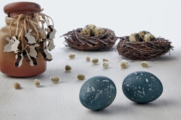 Huevos de gallina pintados y figuritas de madera de liebres en el fondo de nidos de pájaros en un fondo blanco Fondo de tarjeta de Pascua
