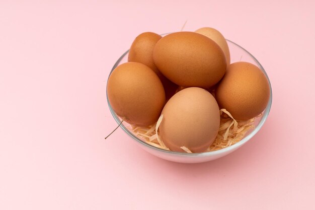 Huevos de gallina en un plato transparente sobre un fondo rosa.