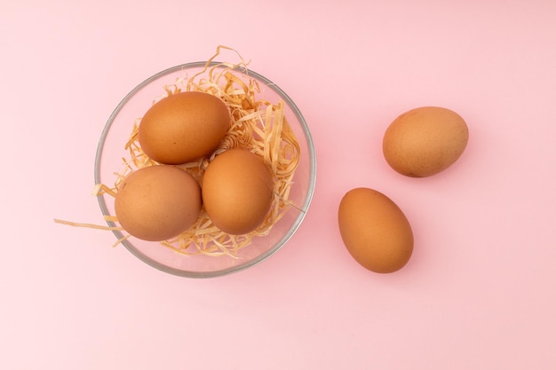 Huevos de gallina en un plato transparente sobre un fondo rosa.