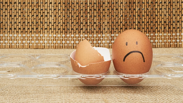 Huevos de gallina en un soporte para huevos. Medio huevo, yema de huevo, cáscara. Emoción y expresión facial pintada en huevos.