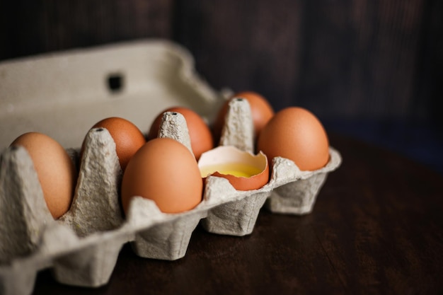 Huevos marrones frescos y un huevo roto con yema en una bandeja ecológica hecha de papel reciclado sobre una madera oscura