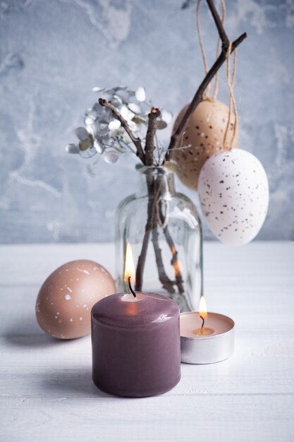 Huevos marrones y velas encendidas en rústica composición de Pascua en mesa de madera blanca.