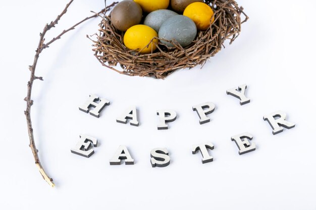 Huevos multicolores en nido de pájaros, rama y la inscripción Felices Pascuas sobre fondo blanco.