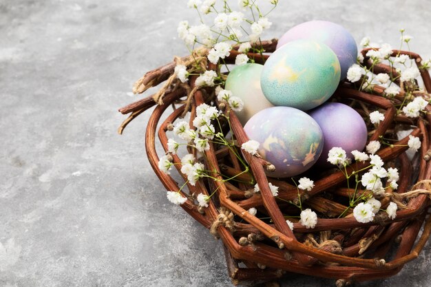 Huevos multicolores para Pascua en el nido con flores sobre fondo gris. Copia espacio Fondo de comida