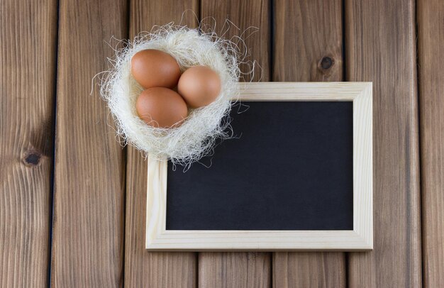 Huevos en un nido con una pizarra sobre una mesa de madera