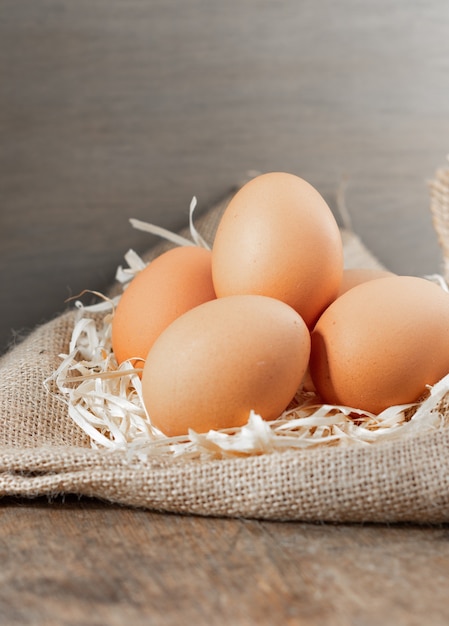 Huevos orgánicos frescos en arpillera con pasto seco sobre mesa de madera.