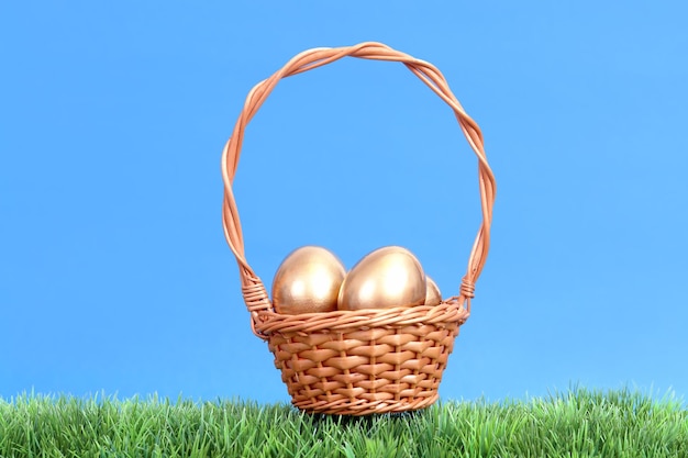 Huevos de oro en una canasta de mimbre en la hierba sobre el cielo azul