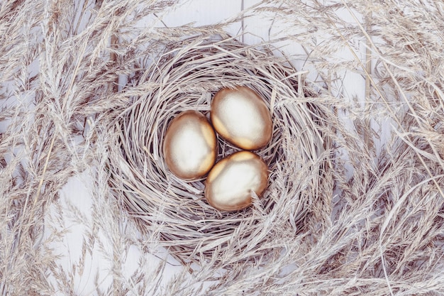 Huevos de oro en un nido de heno Vista aérea de fondo de Pascua en la mesa de madera blanca