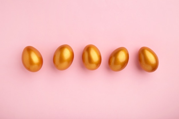 Huevos de oro en la pared rosa pastel. Concepto de pascua.