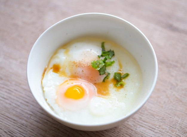 Huevos pasados por agua en un tazón blanco con pimienta cilantro en una mesa de madera huevo desayuno onsen huevo