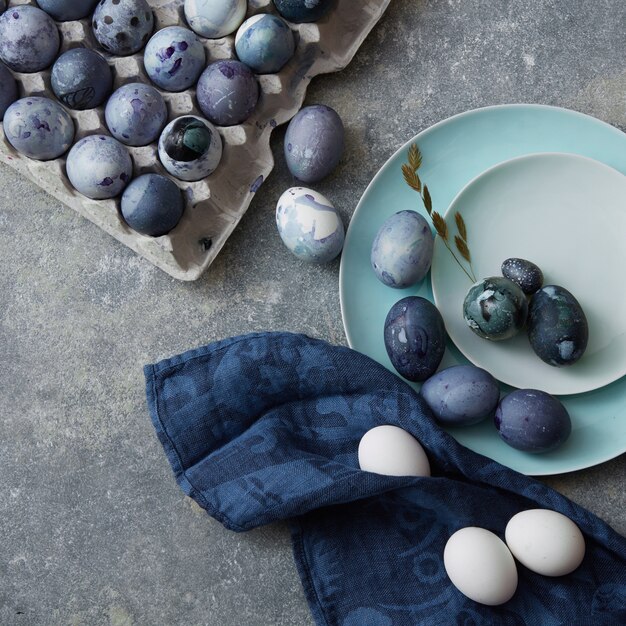 Huevos de Pascua azules con aleteo sobre placas azules y en una caja de papel con una servilleta azul sobre un fondo gris de hormigón se dispara desde arriba